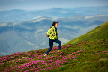 Naklejka na ściany i meble Trekking - woman hiking in mountains on a calm summer day. Woman hiker descending a mountain trail in summer. Flowers in the mountains. Travel concept adventure active vacations outdoor aerial view