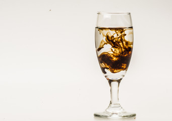 Dark brown food coloring diffuse in water inside wine glass with empty copyspace area for slogan or advertising text message, over isolated grey background. 