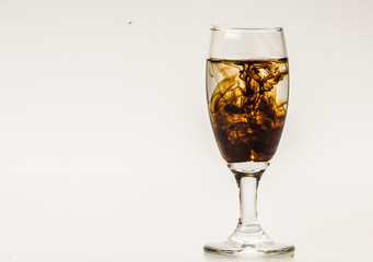Dark brown food coloring diffuse in water inside wine glass with empty copyspace area for slogan or advertising text message, over isolated grey background. 