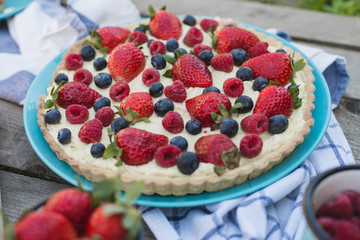 Fruit tart strawberries, blueberries, raspberries on wood in the garden view from above