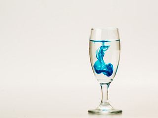 Blue food coloring diffuse in water inside wine glass with empty copyspace area for slogan or advertising text message, over isolated grey background. 