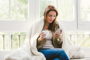 Mature woman using her phone drinking a coffee at home.