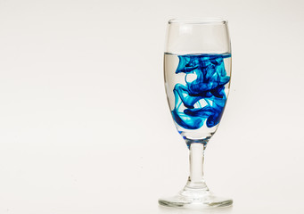 Blue food coloring diffuse in water inside wine glass with empty copyspace area for slogan or advertising text message, over isolated grey background. 