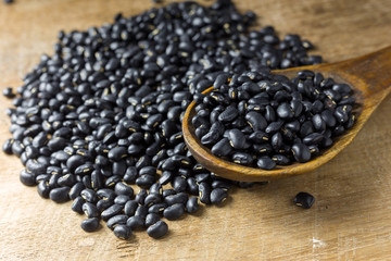 Sack of black beans spill beans with black beans in a wooden spoon on wooden table.