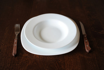 Empty white plate with a fork and knife on a dark wooden brown table
