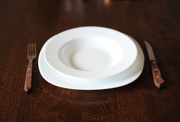 Empty white plate with a fork and knife on a dark wooden brown table