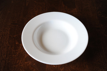 Empty white plate on a dark wooden brown table