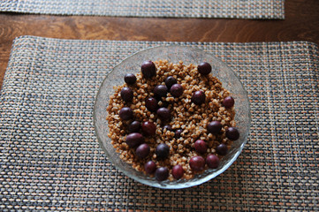 A large glass bowl of boiled buckwheat with grapes gooseberry on a serving napkin