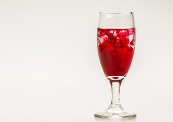 Red food coloring diffuse in water inside wine glass with empty copyspace area for slogan or advertising text message, over isolated grey background. 