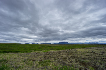 Iceland - Cloudy sky over intense green plant covered meadows and snowy mountains