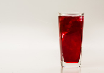 Red food coloring diffuse in water inside glass with empty copyspace area for slogan or advertising text message, over isolated grey background. 