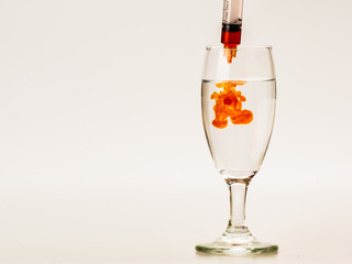 Orange food coloring diffuse in water inside wine glass with empty copyspace area for slogan or advertising text message, over isolated grey background