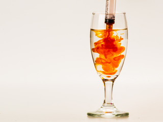 Orange food coloring diffuse in water inside wine glass with empty copyspace area for slogan or advertising text message, over isolated grey background