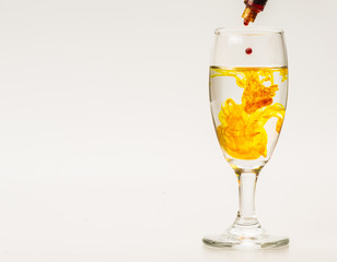 Orange food coloring diffuse in water inside wine glass with empty copyspace area for slogan or advertising text message, over isolated grey background