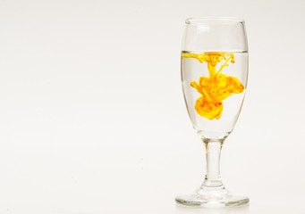 Orange food coloring diffuse in water inside wine glass with empty copyspace area for slogan or advertising text message, over isolated grey background