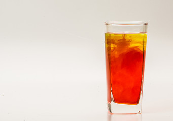 Orange food coloring diffuse in water inside glass with empty copyspace area for slogan or advertising text message, over isolated grey background