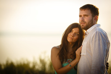 Fototapeta premium A young and beautiful woman laid her hand on her husband's body, a man embraced a woman, enamored spouses looking afar, outside a summer and sunny day