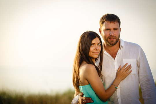 Young and loving couple tenderly embrace each other against the background of nature, husband and wife are looking at the camera, the couple is standing barefoot in the grass