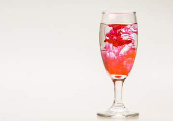mixture of food coloring diffuse in water inside wine glass with empty copyspace area for slogan or advertising text message, over isolated grey background. 