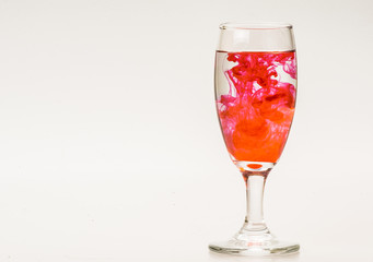 mixture of food coloring diffuse in water inside wine glass with empty copyspace area for slogan or advertising text message, over isolated grey background. 