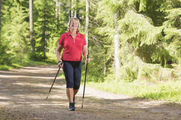 Nordic walking active senior woman working out in the forest and enjoying beautiful summer day. - 168907413