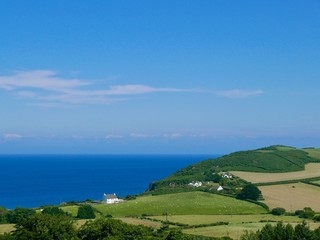 White farmhouse standing amid green fields against the blue sea and sky on the Isle of Man