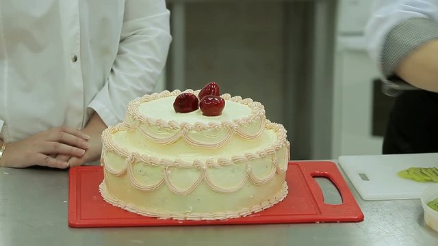 Confectioners cooking cream cake. Placing of jellied strawberry