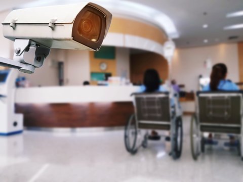 CCTV, security camera system operating record and property protection in hospital with blurred image of patient sitting wheelchair in hospital background, surveillance security technology concept