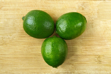 Three green lemons on a wooden plate