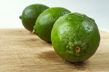 Three green lemons on a wooden plate