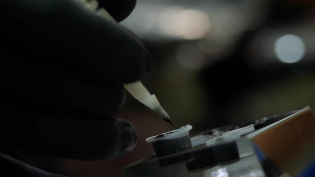 Tattoo artist dipping the machine needle into disposable ink cup. Man working on black gloves in tattoo salon. Slow motion.