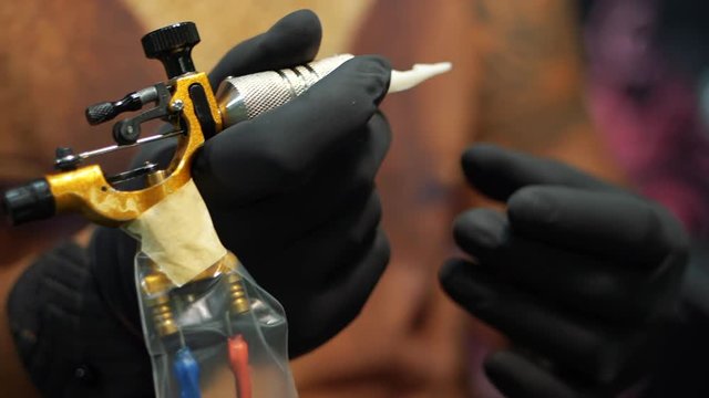 Male artist prepares tools and machine for tattoo session, man holding a tattoo gun. Master works in black sterile gloves. Slow motion. The tattooist checks the machine for performance