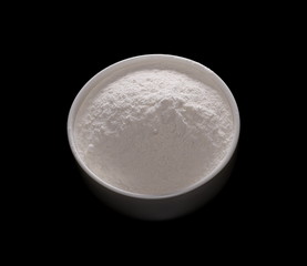 Pile of wheat flour in white bowl isolated on black background