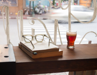 Vintage eyeglasses , books and a glass of beer on wooden counter with daylight from window in the evening. Background outside is the street.
