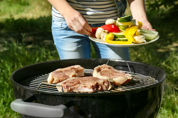 Woman preparing barbecue steaks with vegetables on grill