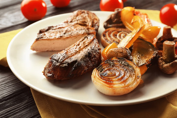 Plate with tasty grilled steak and vegetables on table, close up