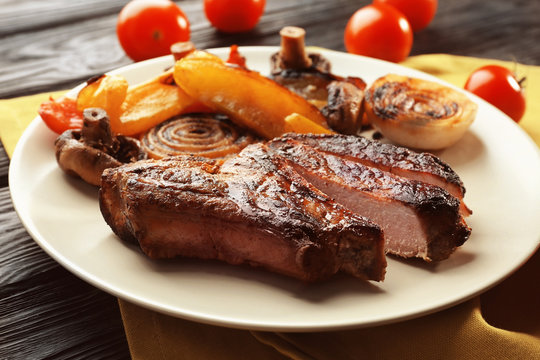 Plate with tasty grilled steak and vegetables on table, close up