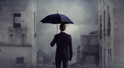 Businessman with umbrella standing over apocalyptic background. Crisis, default, setback concept.