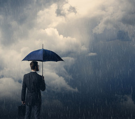 Businessman with umbrella standing over stormy background. Business, protection, crisis concept.