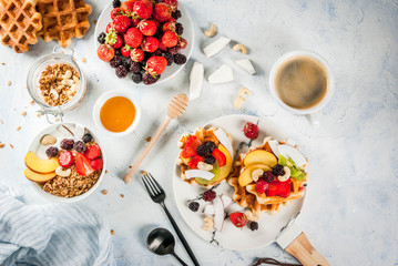Breakfast. Home-made fresh Belgian soft wafers with honey, fresh fruits, nuts and berries; Yoghurt with granola and fruit, a cup of coffee. Light concrete table. Copy space   top view