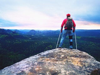 Disabled man with crutches stands on a big rock and looking to mountains at horizon.