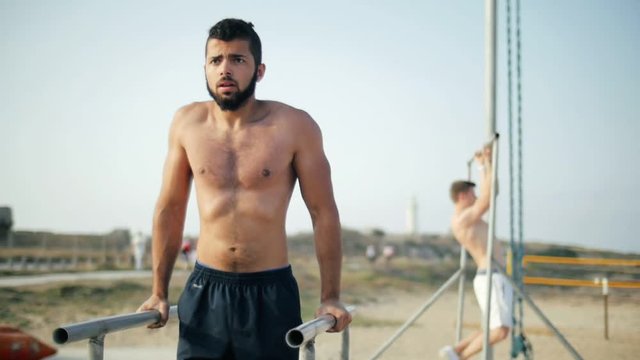 Fitness man pushing on parallel bars. Sportsman doing pull ups on crossbar