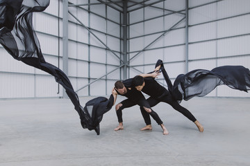 Two male dancers wrestling in a warehouse with black ink-like silk flying around them