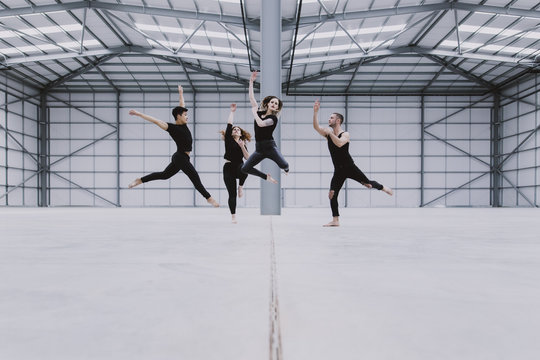 Four dancers jumping at staggered heights in a large empty warehouse