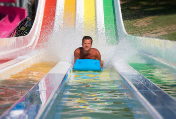 Attraktiver Mann hat Spaß auf einer bunten Wasserrutsche in einem Aquapark