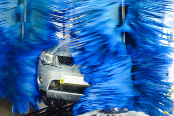 Car wash, black car in automatic car wash, rotating red and blue brush. Washing vehicle.