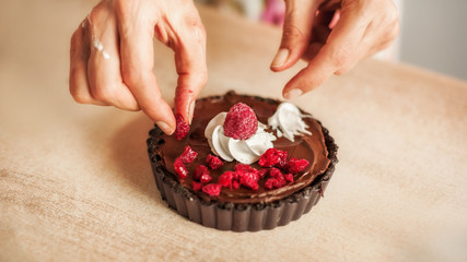 Woman chef preparing chocolate cake with whipped cream and raspberry