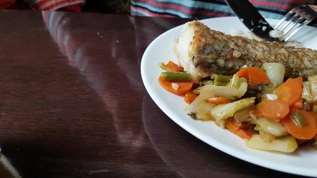 Eating of baked cod with vegetables in restaurant