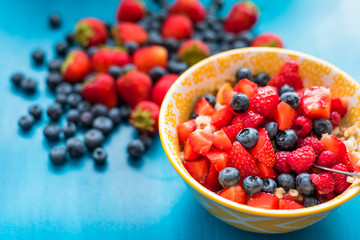 Mix of ripe berries in bowl on white wooden background. Top view.