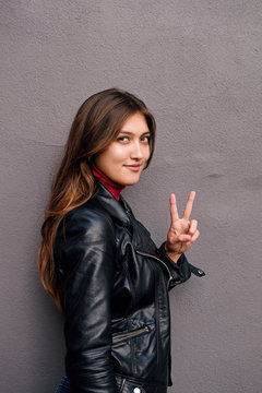 Side view of pretty girl in showing peace sign posing on gray background outdoors. 